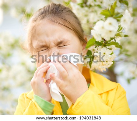 Little girl is blowing her nose near spring tree in bloom