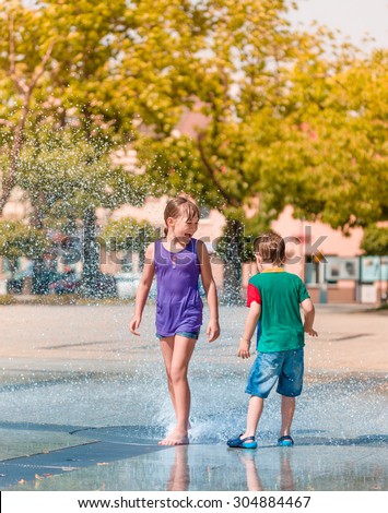 Hot summer in the city - girl and boy are enjoying fountain with cold water