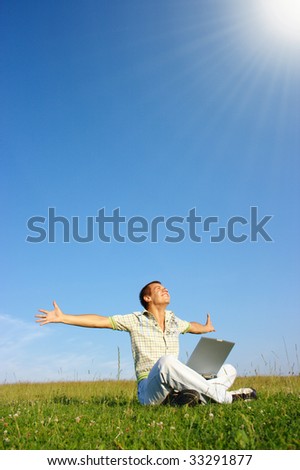 Happy student with laptop on green meadow, sunny day
