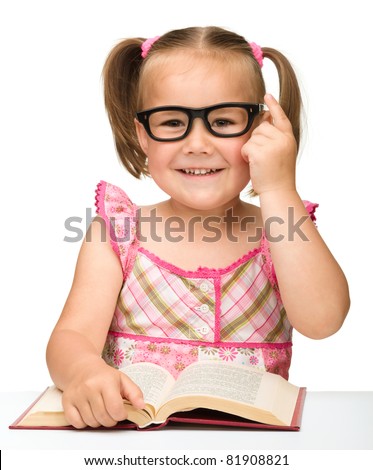 Cute little girl wearing glasses is flipping over pages of a book, isolated on white