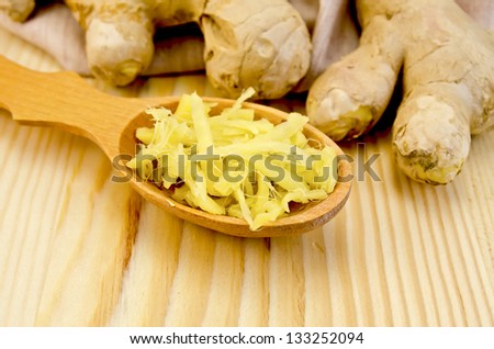 Wooden spoon with grated ginger, ginger root on a napkin on the background of wooden board