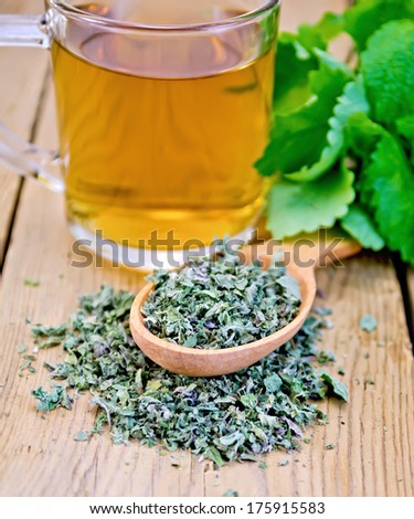 Herbal tea in glass mug, dry mint leaves on a spoon, fresh mint leaves on the background of wooden boards