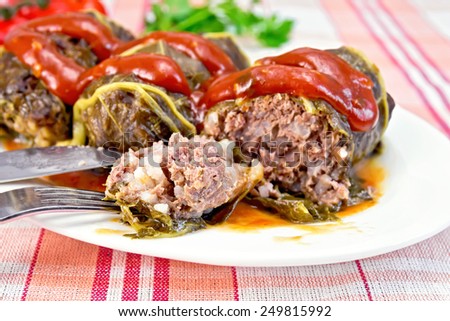 Cabbage rolls with minced meat in the leaves of rhubarb in a plate with tomato sauce, fork, knife on linen background