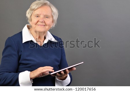 Senior happy woman with tablet against grey background. MANY OTHER PHOTOS WITH THIS SENIOR MODEL IN MY PORTFOLIO.