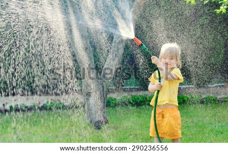 Little girl playing in the garden pouring all the water from a garden hose. MANY OTHER PHOTOS FROM THIS SERIES IN MY PORTFOLIO.