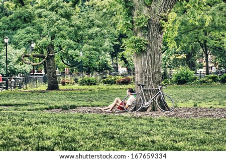 NEW YORK - JUN 14: Biker relaxes under a park tree with his bike, June 14, 2013 in New York. Bike is becoming more and more common in the Big Apple.