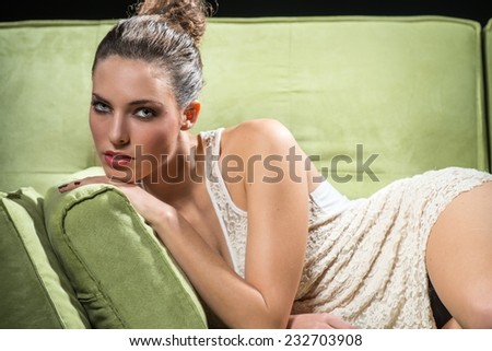 Beautiful young woman laying on the sofa and looking to the camera with enigmatic expression.