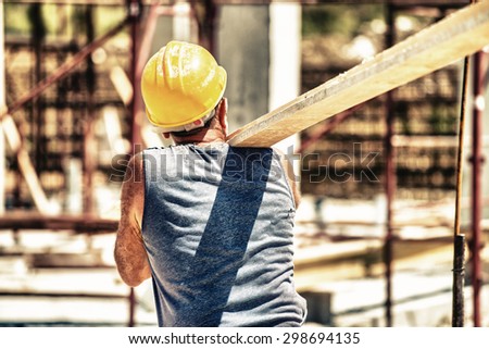 Worker in a construction site transporting a wooden bar.