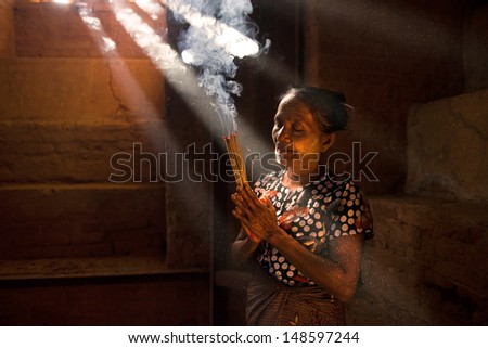 Traditional Old Asian woman praying with incense sticks inside a temple of bagan Myanmar