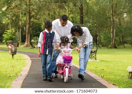 indian family guiding little daughter to cycle