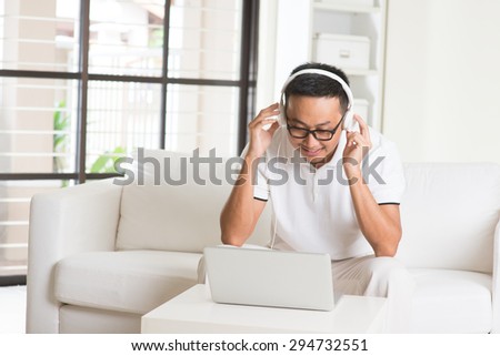 Handsome Asian man using tablet computer. Smiling Southeast Asian college student relaxing and listening to music at home. Asian model.