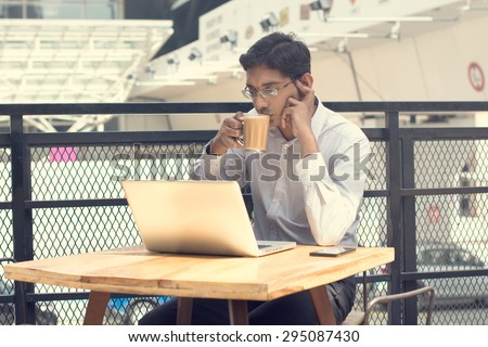 Asian Indian businessman using laptop computer while drinking a cup hot milk tea.