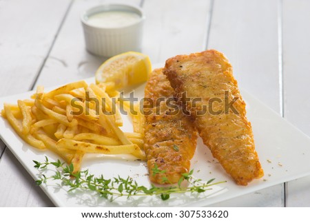 Fish and chips. Fried fish fillet with french fries wrapped by paper cone, on wooden background. Fresh cooked with hot smoke.