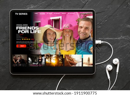 Tablet computer with earphones on black background showing movie and TV shows online streaming service app on the screen