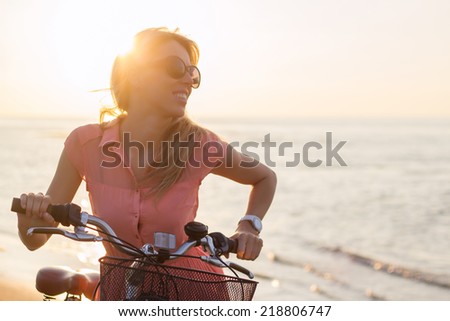 Young fashionable woman riding bicycle on the beach at sunset