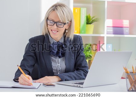 Young business woman writing to do list while sitting at her desk