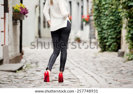 Fashionable woman in city wearing black pants and red high heel shoes.