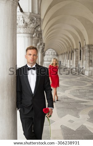 Elegantly dressed man holding rose in hand and waiting for his date