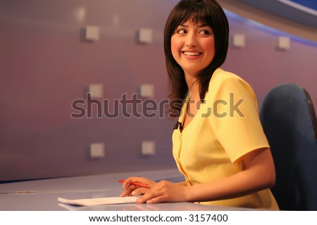 Young woman TV reporter smiling and looking back while preparing for the news presenting