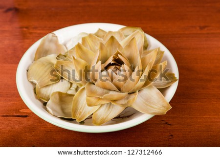 A close up of an artichoke  that has been steamed and is folded open like a flower in a bowl on a wooden table.