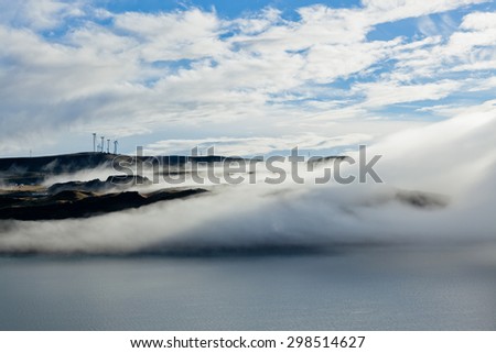 Creeping fog rolls over the Columbia River Gorge and obscures the landscape of the Oregon river bank.