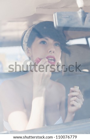 woman looking in rear view mirror and putting make up in car