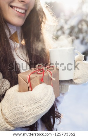 woman drinks tea and holds a gift in hand on a background of a winter landscape, outdoor
