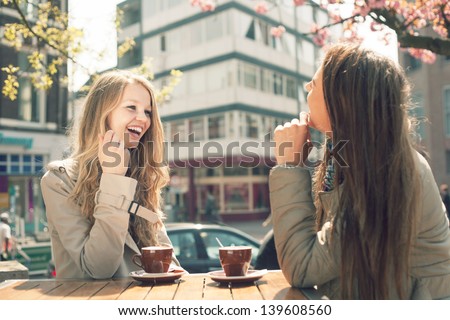 Two young women talk and drink coffee in cafe, outdoors