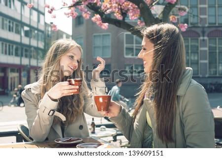 Two pretty girl-friends talk and drink tea in cafe, outdoors