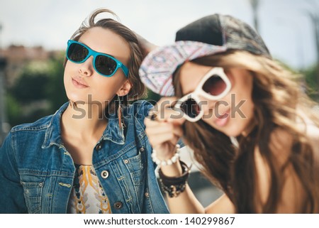 Two happy girls in sunglasses looking into the distance on the urban background. Young active people. Outdoors