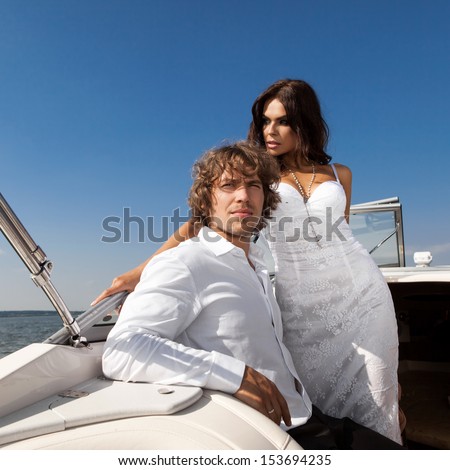 lovely beautiful couple posing on the luxury boat in open sea in summer. Young man and sensual brunette outdoor portrait in classic dress near the ocean. Outdoors, lifestyle.