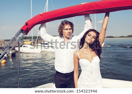 Fashion lovely beautiful couple relaxing on the luxury boat in open sea in summer. Young man and sensual brunette outdoor portrait in classic dress. Outdoors, lifestyle.