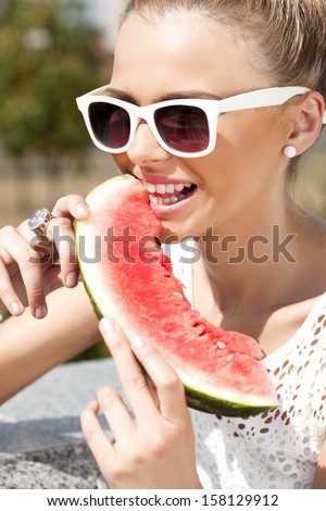 Woman biting watermelon from the opened fridge full of vegetables and fruit. Concept of healthy and dieting food