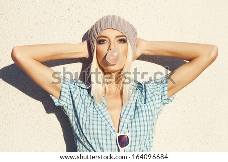 trendy beautiful blonde  in   blue shirt posing on wall background. Blow bubblegum. Outdoors, lifestyle.