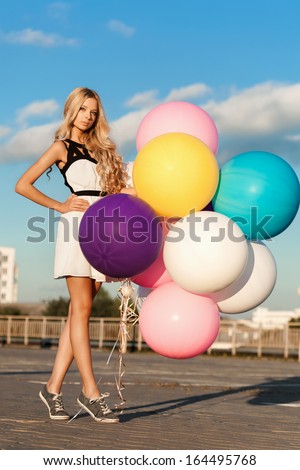 Happy young woman standing with  big colorful latex balloons.  Gorgeous thick wavy hair. Outdoors, lifestyle