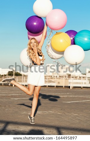 Happy young blonde having fun with big colorful latex balloons.  Gorgeous thick wavy hair. Outdoors, lifestyle