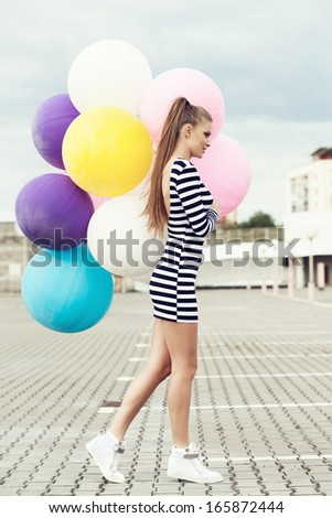 Happy young woman walking with big colorful latex balloons. Outdoors, lifestyle