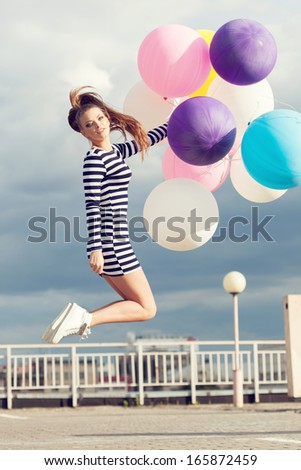 Happy young beautiful woman jumping with colorful latex balloons. Outdoors, lifestyle