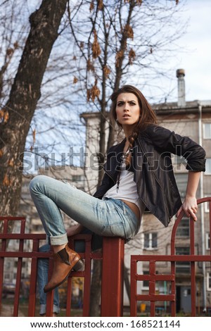 Portrait of a beautiful girl hipster. Naughty woman sitting on the fence. Outdoors, lifestyle.