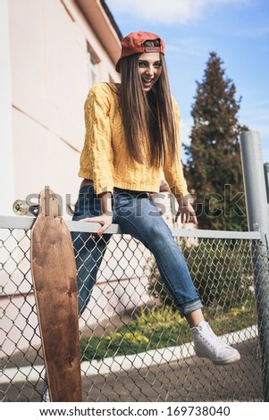 Beautiful young girl with longboard sitting on the fence in the afternoon, outdoor