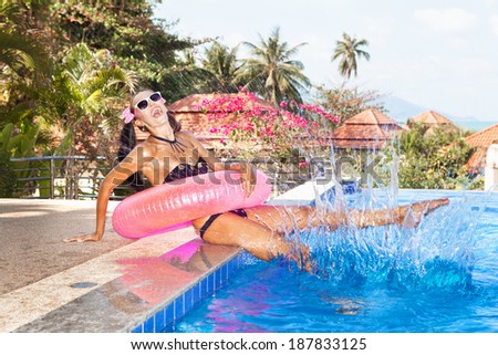 Young woman in bikini and white sunglasses with pink inner tube having fun near pool. Outdoors