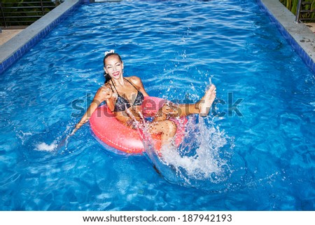 naughty girl floating in an pink inner tube in a swimming pool and laughing. Outdoor portrait of girl having fun.