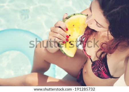 Young woman eating watermelon against swimming pool