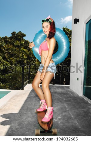 Young woman having fun near swimming pool on longboard with inner tube. Outdoors