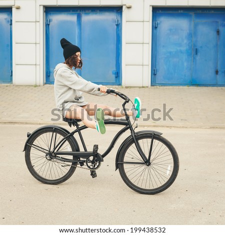Young hipster girl riding black bike