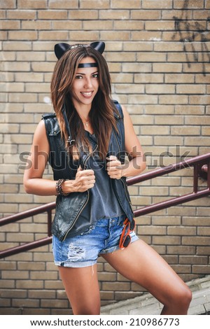 Bad sexy woman with leather cat ears showing tongue. Urban scene. Outdoor lifestyle portrait
