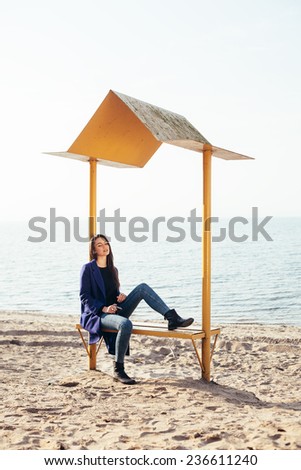 Outdoor portrait of young pretty woman posing near the sea alone, sitting and waiting
