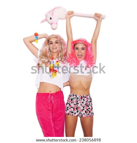 Funny girl friends in pink wigs and clothing have fun with a unicorn on white background not isolated