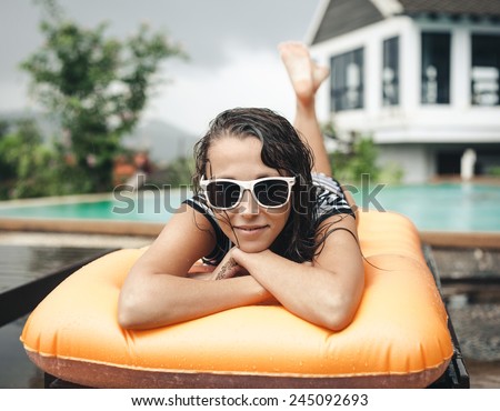 Young woman lying on an inflatable mattress near the pool. Cute girl in sunglasses resting wet from rain