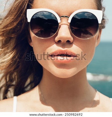 Closeup fashion summer portrait of pretty young woman in sunglasses posing on the beach on vacation